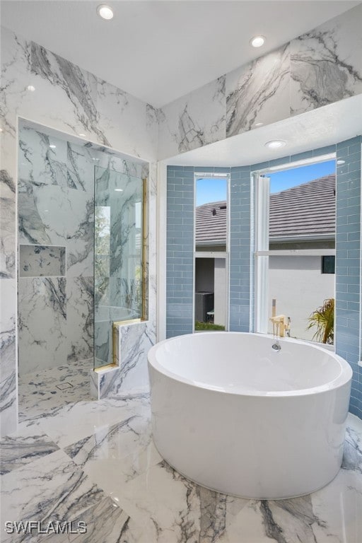 full bath with recessed lighting, marble finish floor, stone wall, and a soaking tub