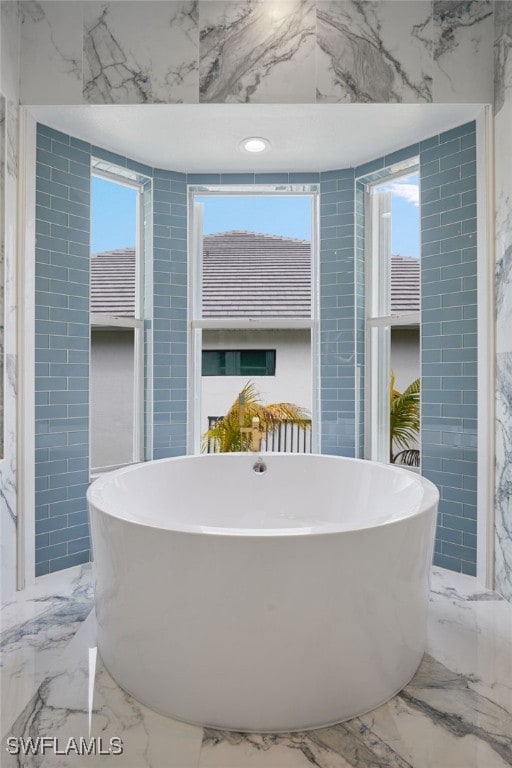 full bathroom with a soaking tub, tile walls, and marble finish floor