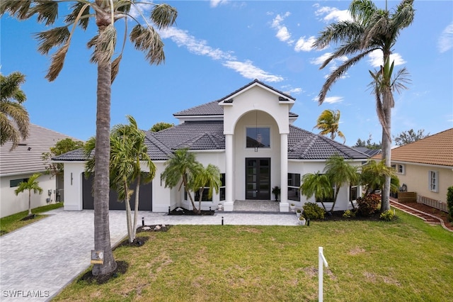 mediterranean / spanish home featuring a front yard, an attached garage, stucco siding, a tiled roof, and decorative driveway