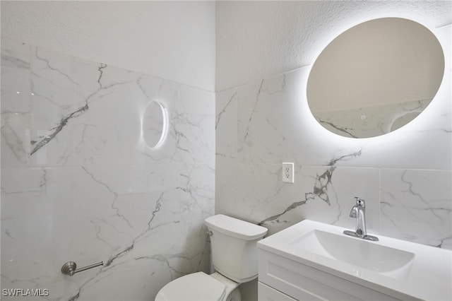 bathroom with toilet, vanity, stone wall, and a textured wall