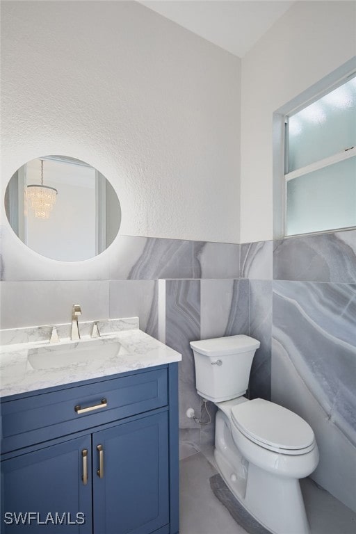 bathroom featuring tile walls, a notable chandelier, toilet, and vanity