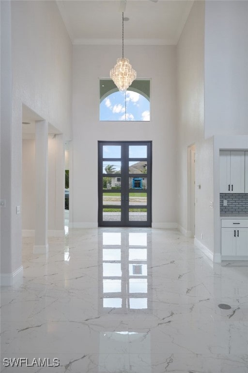 foyer entrance featuring marble finish floor, french doors, an inviting chandelier, and ornamental molding