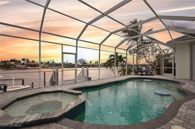 pool at dusk with glass enclosure, a patio area, and a pool with connected hot tub