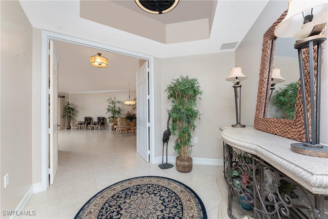 hallway featuring a tray ceiling, light tile patterned flooring, visible vents, and baseboards