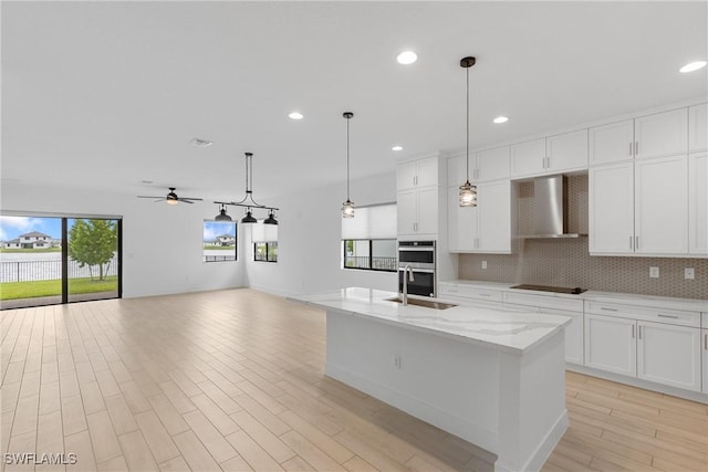 kitchen featuring decorative backsplash, wall chimney exhaust hood, open floor plan, stainless steel double oven, and a sink