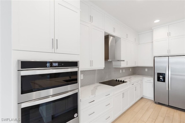 kitchen with decorative backsplash, wall chimney exhaust hood, appliances with stainless steel finishes, light stone counters, and white cabinetry