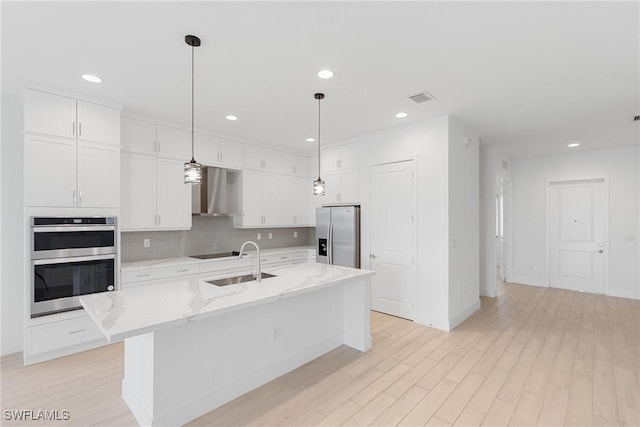 kitchen with appliances with stainless steel finishes, white cabinets, a sink, and wall chimney range hood