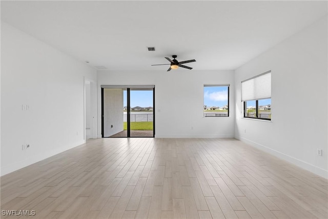 spare room featuring a ceiling fan, light wood-type flooring, visible vents, and plenty of natural light