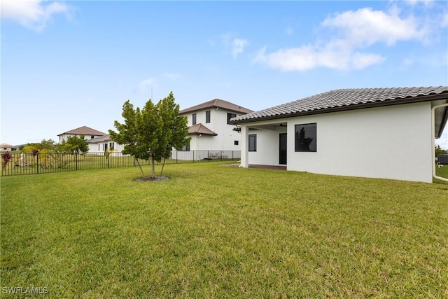 back of house with stucco siding, a tile roof, fence, and a yard