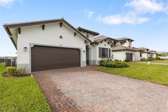 mediterranean / spanish-style home with stucco siding, an attached garage, fence, decorative driveway, and a front yard