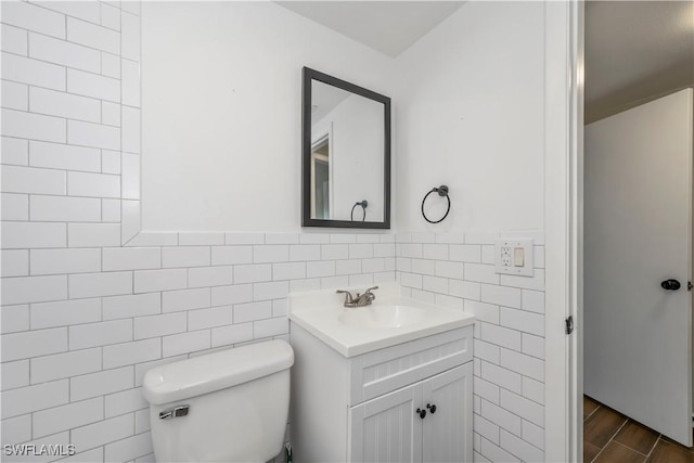 bathroom featuring tile walls, toilet, wainscoting, vanity, and wood finished floors