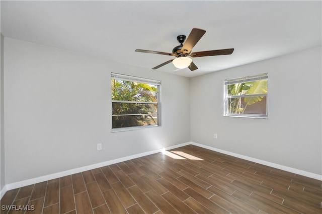 spare room with dark wood-type flooring, a ceiling fan, a wealth of natural light, and baseboards