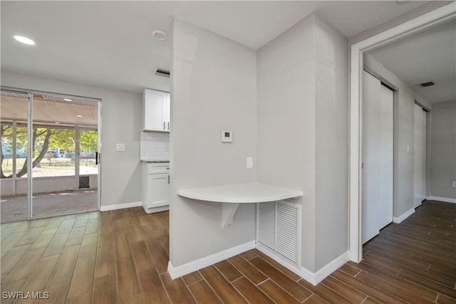 hall featuring dark wood-type flooring, visible vents, and baseboards