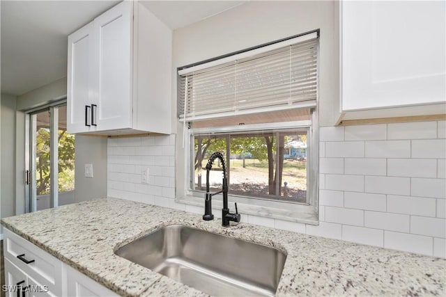 kitchen featuring light stone countertops, white cabinetry, backsplash, and a sink