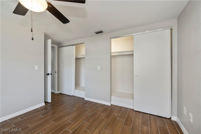 unfurnished bedroom featuring wood finish floors, visible vents, baseboards, and two closets