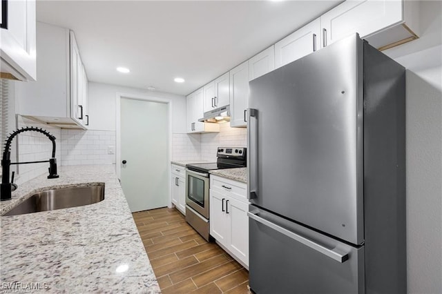 kitchen featuring white cabinets, stainless steel appliances, wood finish floors, under cabinet range hood, and a sink