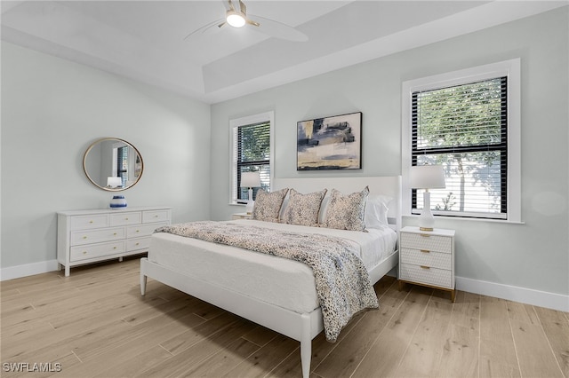 bedroom featuring baseboards, a raised ceiling, and light wood-style floors