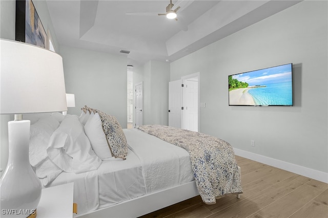 bedroom featuring a tray ceiling, ceiling fan, ensuite bath, wood finished floors, and baseboards