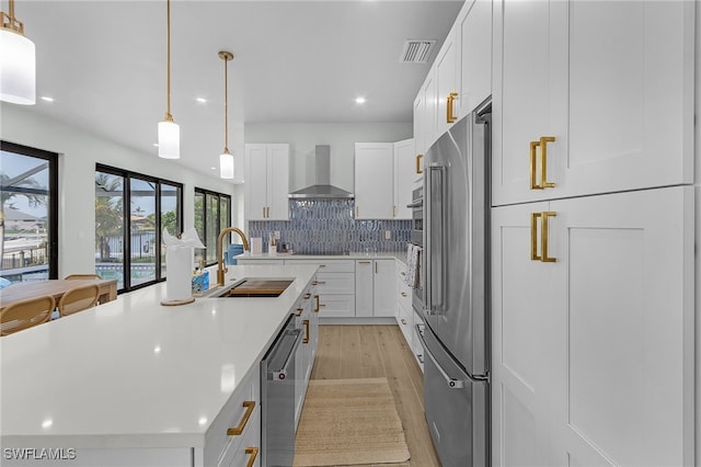 kitchen with stainless steel appliances, visible vents, decorative backsplash, a sink, and wall chimney exhaust hood