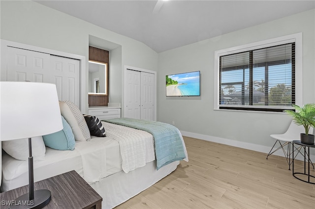 bedroom featuring baseboards, light wood finished floors, lofted ceiling, and multiple closets