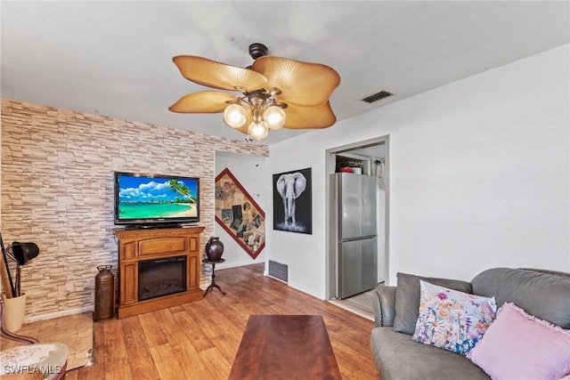 living area featuring a glass covered fireplace, a ceiling fan, visible vents, and light wood-type flooring