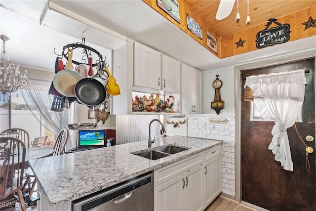 kitchen with a sink, light stone countertops, dishwasher, and white cabinets