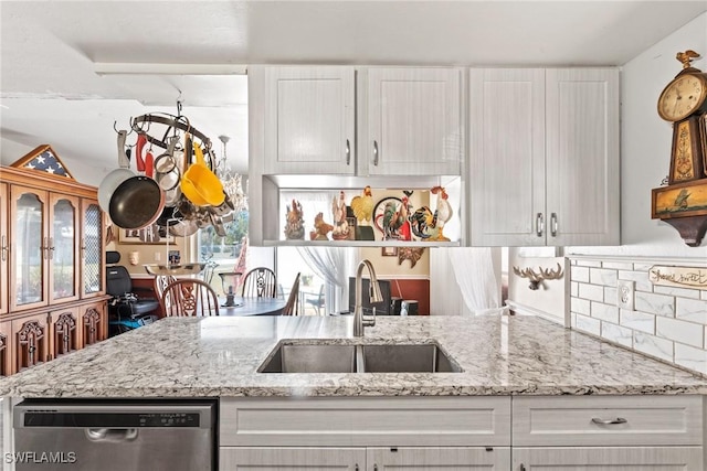 kitchen featuring light stone counters, white cabinetry, a sink, dishwasher, and backsplash