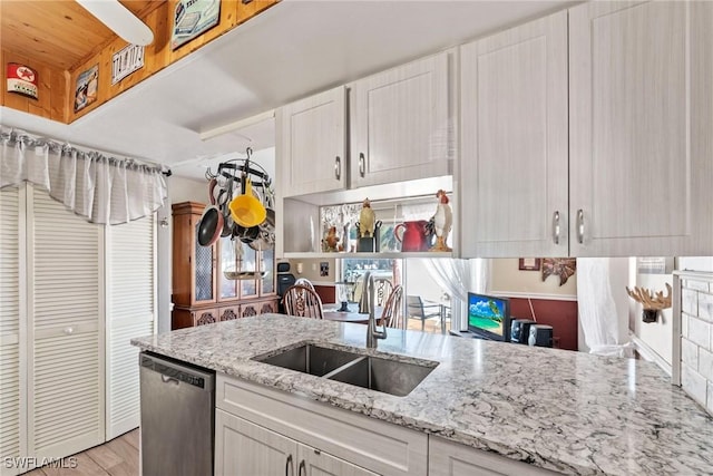 kitchen with light stone counters, white cabinetry, a sink, stainless steel dishwasher, and light wood-type flooring