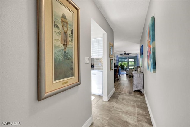 hall featuring light tile patterned flooring and baseboards