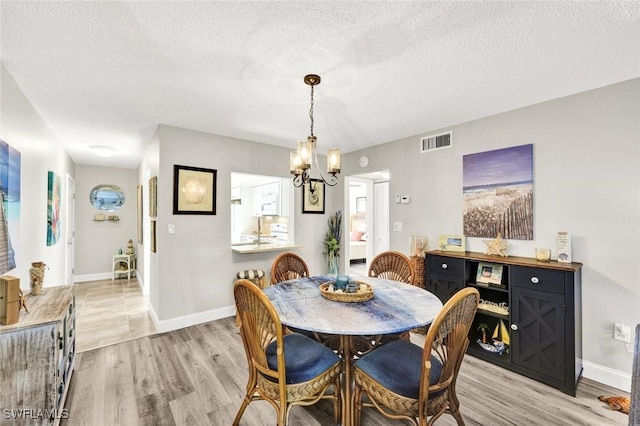 dining space with baseboards, light wood-style floors, visible vents, and a textured ceiling