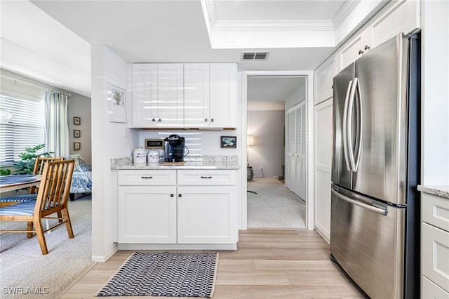 kitchen featuring visible vents, ornamental molding, light wood-style flooring, freestanding refrigerator, and white cabinets