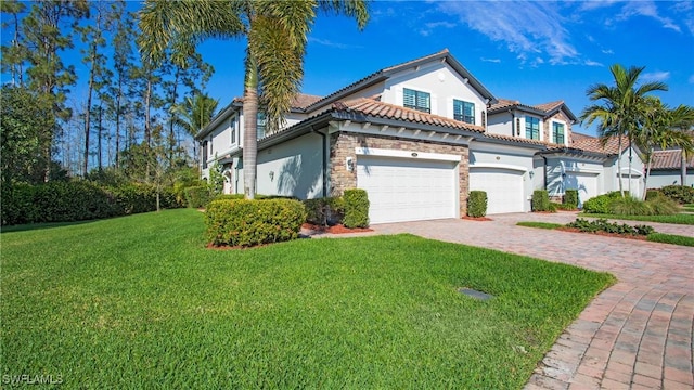 mediterranean / spanish-style home featuring driveway, stucco siding, a front lawn, stone siding, and a tile roof