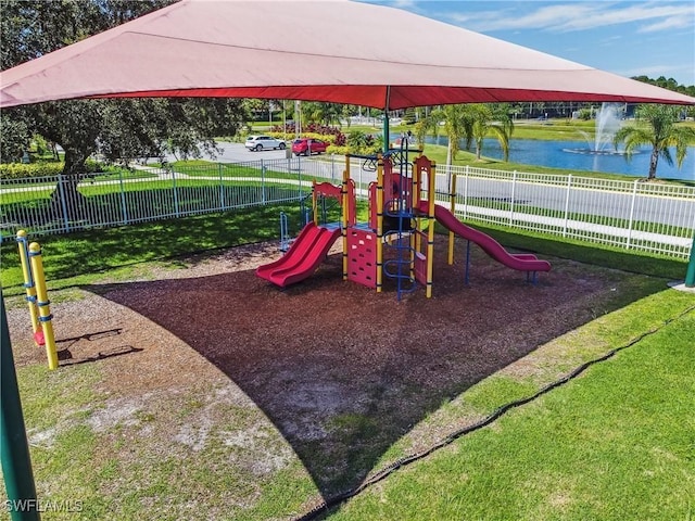 community playground featuring fence, a lawn, and a water view