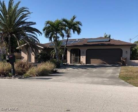 ranch-style home with roof mounted solar panels, stucco siding, an attached garage, and driveway