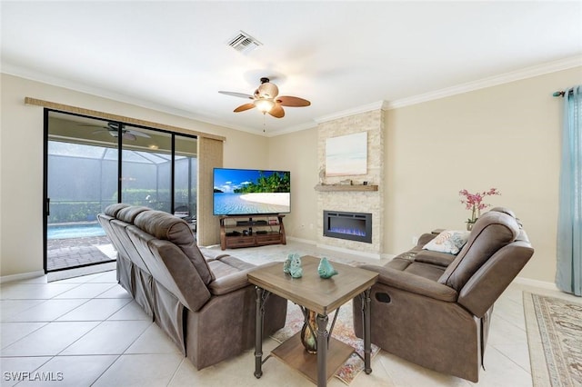 living area with light tile patterned floors, ceiling fan, ornamental molding, and a stone fireplace