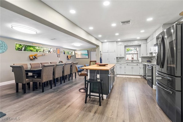 kitchen featuring a breakfast bar area, a sink, white cabinets, appliances with stainless steel finishes, and wood counters