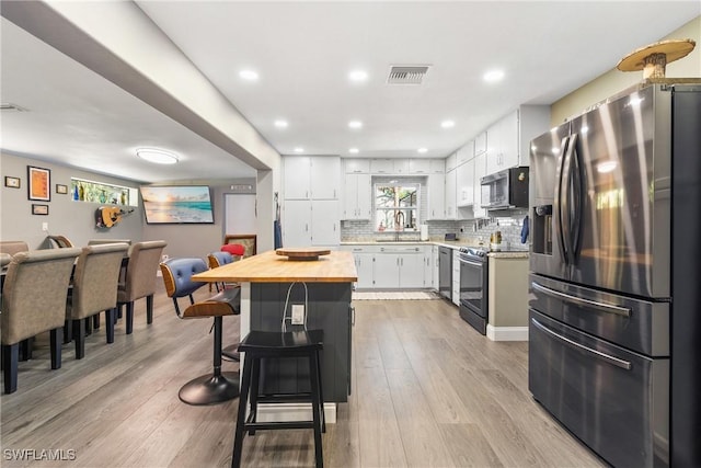 kitchen with wooden counters, a breakfast bar, appliances with stainless steel finishes, white cabinetry, and a sink