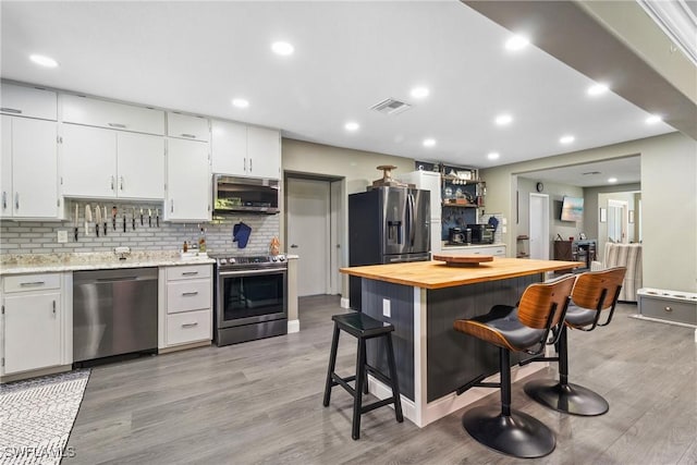 kitchen with visible vents, butcher block countertops, a kitchen bar, white cabinets, and stainless steel appliances