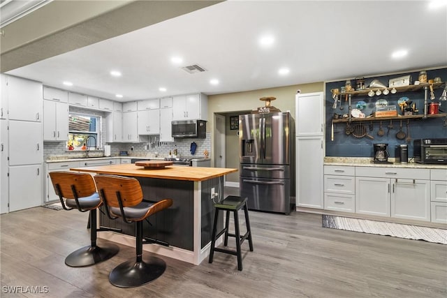 kitchen featuring visible vents, white cabinets, appliances with stainless steel finishes, wood counters, and a kitchen breakfast bar