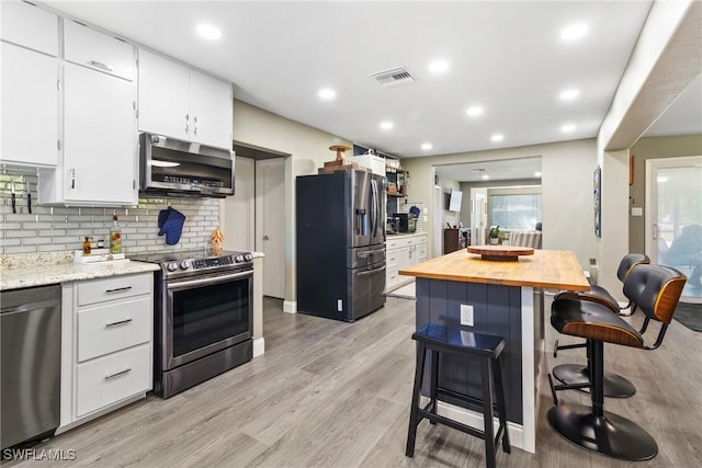 kitchen with visible vents, butcher block countertops, a kitchen breakfast bar, white cabinetry, and appliances with stainless steel finishes