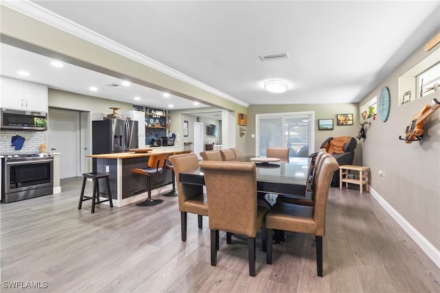 dining room featuring crown molding, light wood-style floors, visible vents, and baseboards