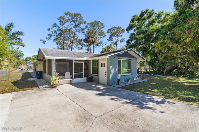 view of front of home with a front lawn, a patio, fence, concrete driveway, and a sunroom