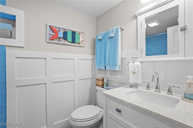 bathroom with toilet, vanity, a decorative wall, and wainscoting