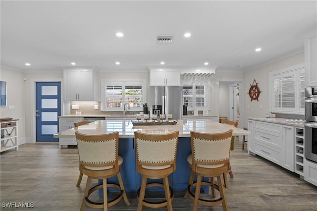 kitchen featuring stainless steel appliances, white cabinetry, visible vents, ornamental molding, and a center island