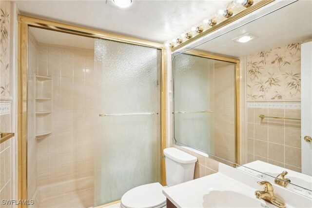 bathroom featuring wallpapered walls, toilet, vanity, a shower stall, and tile walls