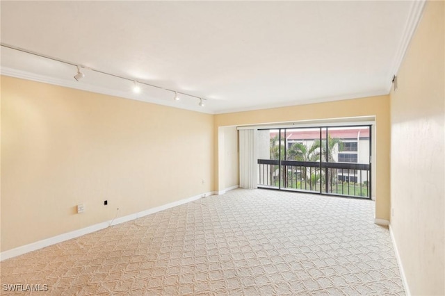 empty room featuring light colored carpet, rail lighting, crown molding, and baseboards