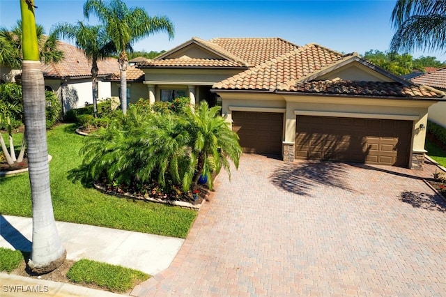 mediterranean / spanish-style home with a tile roof, stucco siding, decorative driveway, stone siding, and an attached garage