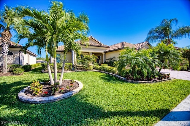 mediterranean / spanish home with a front yard, a tiled roof, a garage, and stucco siding