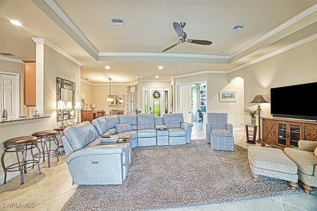 living area featuring a raised ceiling, decorative columns, a ceiling fan, and visible vents