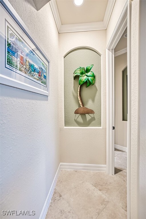 hallway featuring a textured wall, baseboards, and ornamental molding